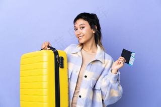 一位年轻的乌拉圭妇女带着旅行箱和护照在紫墙上度假