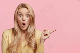 吓坏了的年轻女人会警告你一些事情，用食指指着一边，张大嘴巴，用窃听的眼睛盯着你，孤立在粉红色墙上的广告概念上