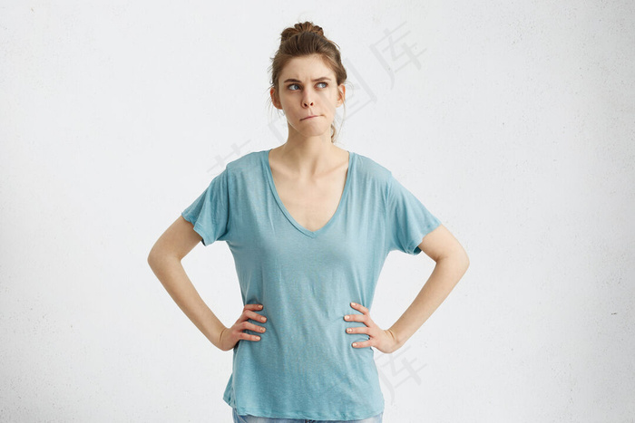 一个沉思的、怀疑的高加索人女孩侧视着，感到犹豫不决和不确定，因为她必须对工作问题做出重要的决定，嘴唇紧闭，手放在腰上