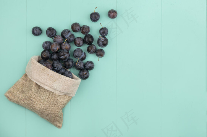 蓝色背景的粗麻袋上的黑色球形涩味小浆果的俯视图