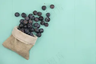蓝色背景的粗麻袋上的黑色球形涩味小浆果的俯视图