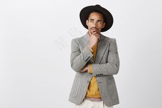 努力寻找解决办法，让生活更美好。身着时尚服饰，头戴黑色帽子，目光集中，富有魅力的非洲男性，抚摸着下巴，抬起头，表情深思熟虑，思考或回忆重要事件