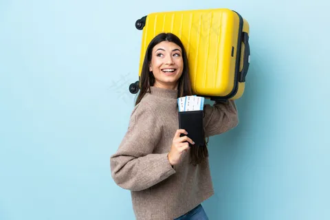一个年轻的黑发女孩带着手提箱和护照在蓝色的墙上度假