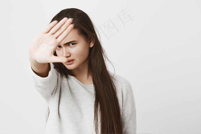 一位长发乌黑的少女的特写镜头，用手做停止手势，皱着眉头。