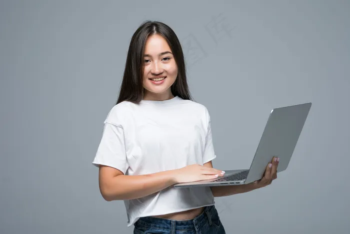 一位亚洲妇女拿着笔记本电脑看着灰色背景的相机