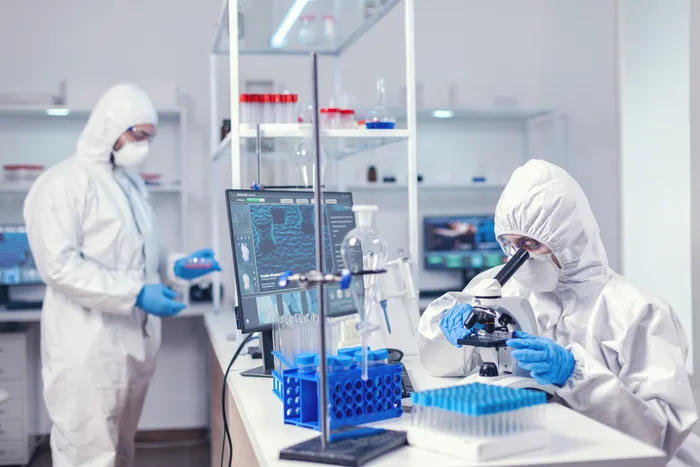 穿着个人防护服对抗冠状病毒的医学科学家团队正在努力寻找治疗方法。全球大流行期间的化学家研究员，在生物化学实验室使用 covid-19 检查样本