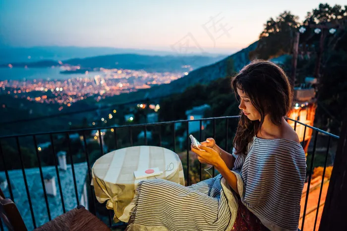 女人坐在阳台上，背景是夜市