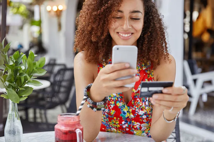 美丽的非裔美国女人的短镜头，拥有现代手机和信用卡，在网上购物