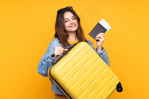 年轻的白人妇女在黄色的墙上度假，带着手提箱和护照