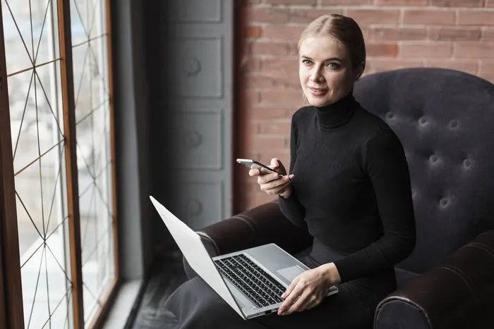 沙发上的女人拿着笔记本电脑和手机