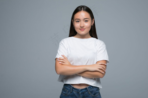 情感概念。愤怒可爱的亚洲女人站在那里，交叉双臂，看着白色背景下灰色衣服的相机