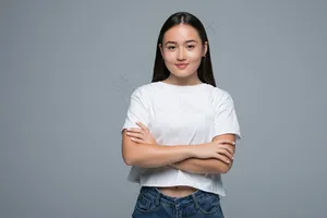 情感概念。愤怒可爱的亚洲女人站在那里，交叉双臂，看着白色背景下灰色衣服的相机