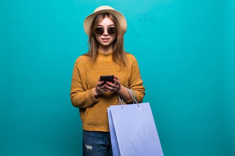 年轻的女人戴着绿色的帽子，戴着墨镜在墙上购物