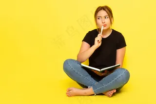 一位年轻女性坐在黑色衬衫和蓝色牛仔裤上写下笔记，思考黄色