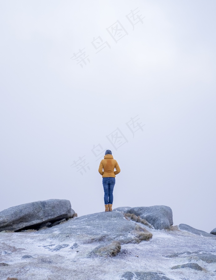 雪山中一位身穿黄色外套的女性站在石头上的垂直镜头
