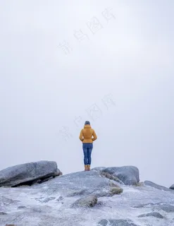 雪山中一位身穿黄色外套的女性站在石头上的垂直镜头 雪山中一位身穿黄色外套的女性站在石头上的垂直镜头