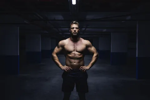 四分之三长度的无上装肌肉运动员短裤站在车库，双手放在臀部。城市生活理念。