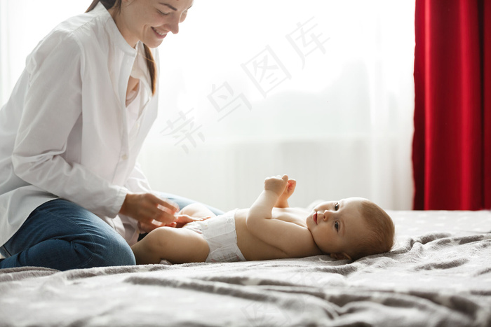 明亮卧室里快乐的年轻妈妈微笑着给她宝贝的儿子穿上衣服去公园散步。家庭观念。。