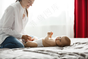 明亮卧室里快乐的年轻妈妈微笑着给她宝贝的儿子穿上衣服去公园散步。家庭观念。。
