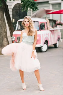 穿着浅薄纱裙、金色长发、复古汽车背景的时尚模特。她正看着镜头。