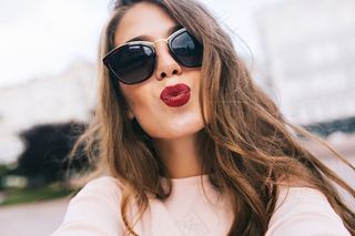 城市中戴墨镜留长发的美女特写照。她用酒红色的嘴唇吻了一下。