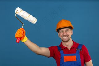 年轻的建筑工人穿着建筑制服，戴着安全帽，手持油漆辊，脸上挂着灿烂的笑容