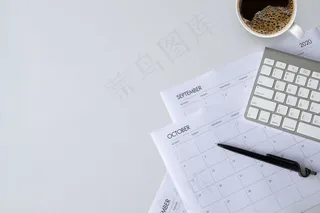 办公桌俯视图，白色桌子上有咖啡杯、键盘和工作时间表