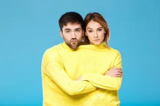 一对穿着黄色毛衣的情侣在蓝色的墙上交叉双臂