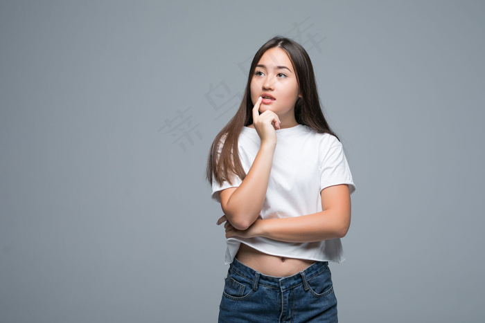 年轻的亚洲女人在灰色的背景下孤立无援地看着一边。