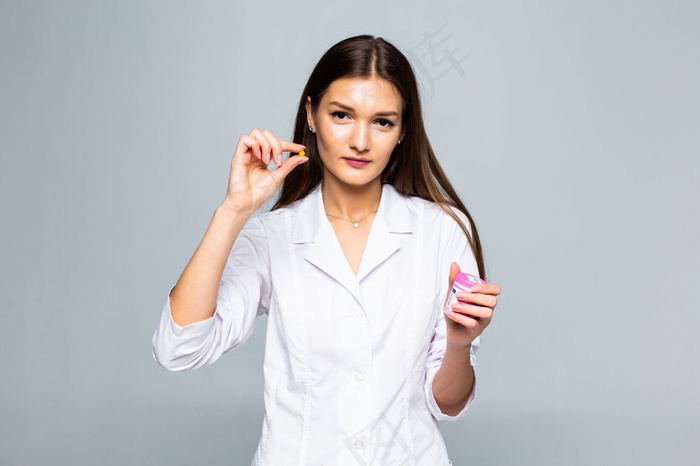微笑的女医生拿着隔离在白墙上的药丸。