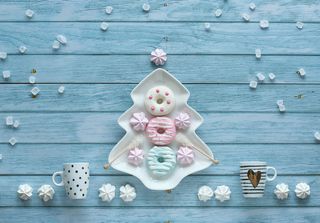 抽象装饰圣诞背景与糖果，咖啡杯，棉花糖，甜甜圈和糖晶体。圣诞树形状的盘子和糖果排列在质朴的蓝色木质背景上。