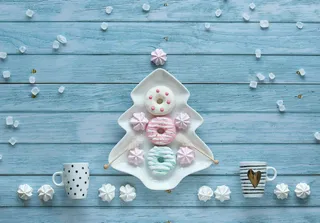 抽象装饰圣诞背景与糖果，咖啡杯，棉花糖，甜甜圈和糖晶体。圣诞树形状的盘子和糖果排列在质朴的蓝色木质背景上。