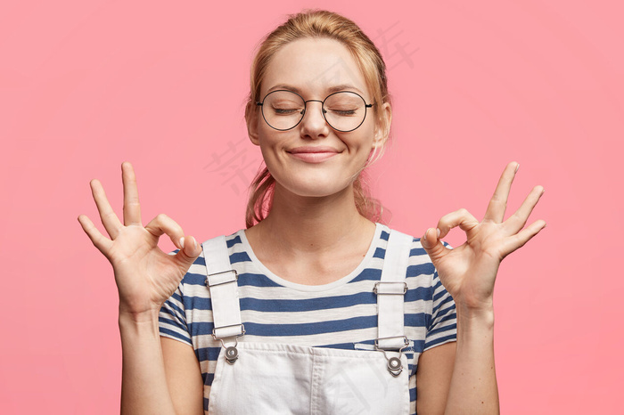 满意的金发美女迷人的快乐女性的肖像表示ok标志，闭上眼睛，心情愉快，周末快乐，与粉色隔离