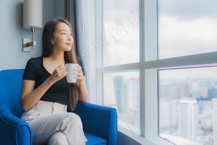 肖像美丽的年轻亚洲女人拿着咖啡杯坐在客厅的沙发椅上