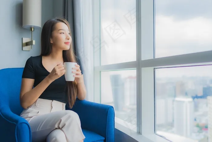 肖像美丽的年轻亚洲女人拿着咖啡杯坐在客厅的沙发椅上