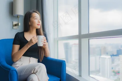 肖像美丽的年轻亚洲女人拿着咖啡杯坐在客厅的沙发椅上 肖像美丽的年轻亚洲女人拿着咖啡杯坐在客厅的沙发椅上