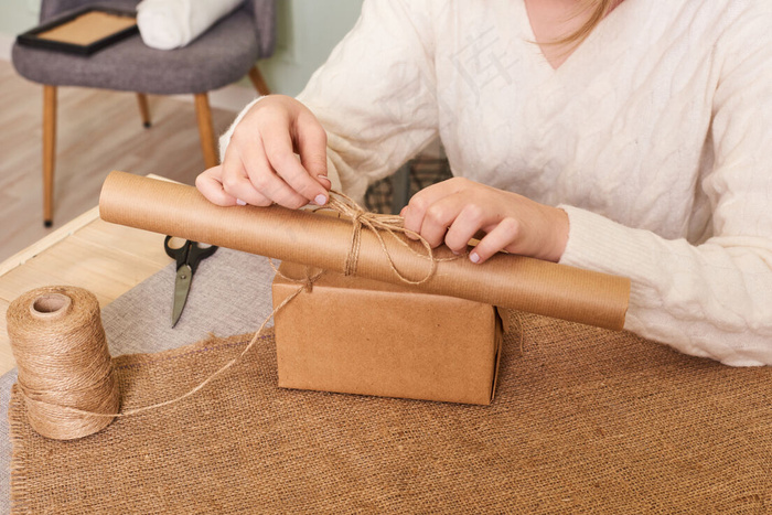 重点放在女人手上的白色针织毛衣包装盒里。手工包装纸和天然绳线。节日礼物，惊喜。节礼日礼物