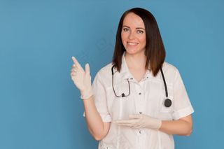 戴着医用手套的快乐女医生用听诊器指着复印空间。医疗保健理念