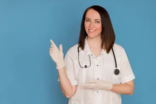 戴着医用手套的快乐女医生用听诊器指着复印空间。医疗保健理念