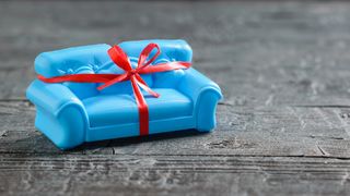 黑色木地板上系着红色礼品带的蓝色沙发。不寻常的礼物。