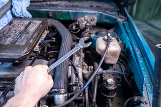 一个年轻的汽车修理工手里拿着扳手，正准备在汽车引擎盖下修理汽车。汽车修理和汽车修理厂的概念