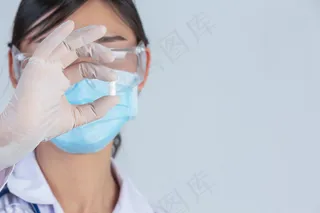 年轻漂亮的医生戴着口罩，手里拿着药，灰色的墙上戴着橡胶手套。