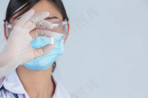 年轻漂亮的医生戴着口罩,手里拿着药,灰色的墙上戴着橡胶手套。 年轻漂亮的医生戴着口罩,手里拿着药,灰色的墙上戴着橡胶手套。
