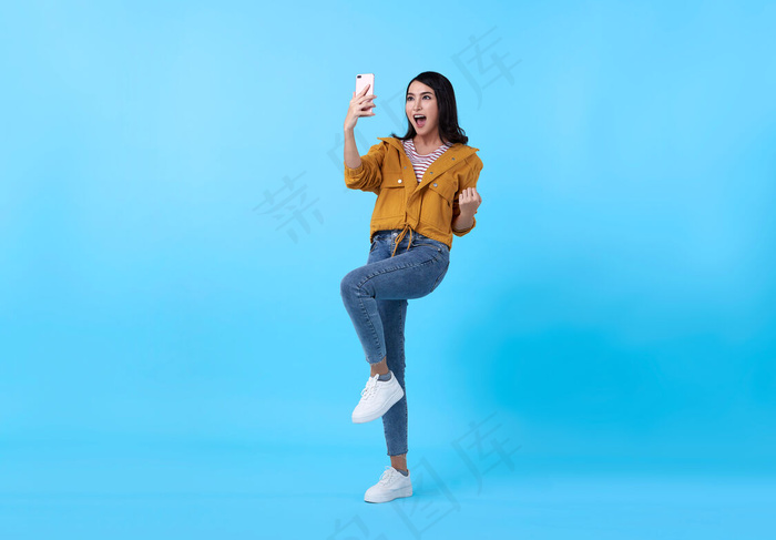 一位快乐的年轻亚洲女性的画像，在蓝色背景下用手机隔离庆祝。