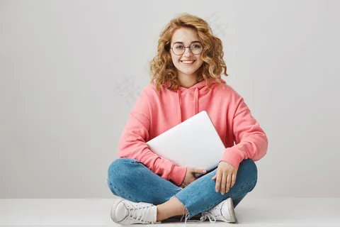 活泼聪明的女学生坐在地板上，手里拿着笔记本电脑