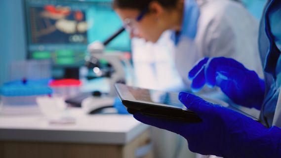 关闭科学家在平板电脑上写作,而生物学家团队深夜在 backgorund 显微镜下进行生物研究 关闭科学家在平板电脑上写作,而生物学家团队深夜在 backgorund 显微镜下进行生物研究