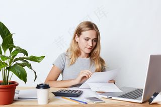 年轻女商人用笔记本电脑和计算器工作，聚精会神地看文件，计算公司账单，做财务报告。人、职业和商业理念