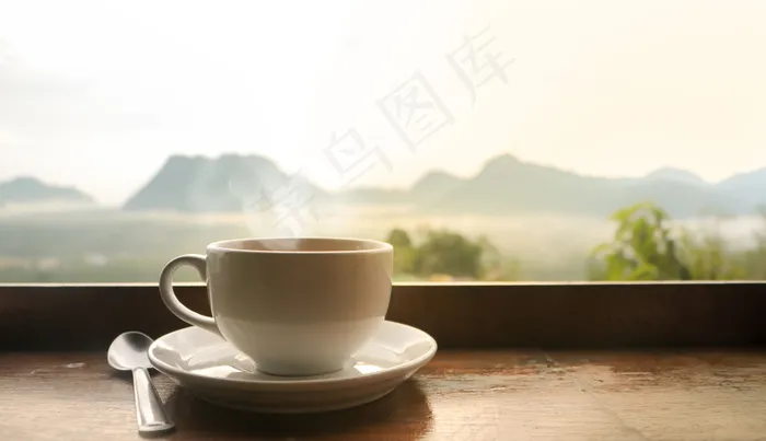 清晨，白色陶瓷咖啡杯放在木桌上，阳光照在朦胧的山景上