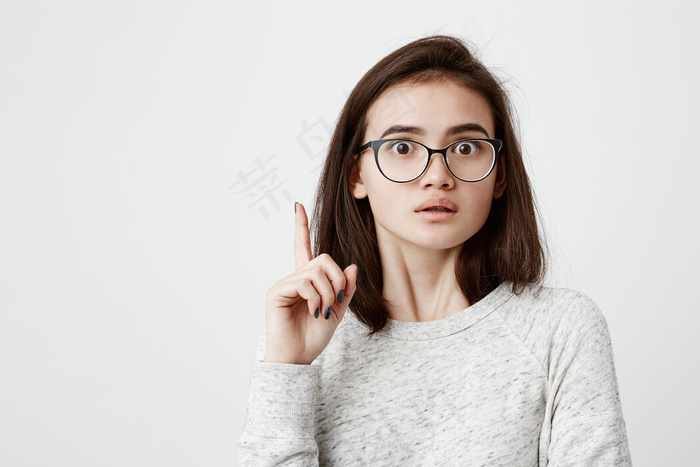 我有一个好主意聪明聪明的黑发美女，戴着眼镜，手指朝上。可爱的小女孩，眼睛突出，用食指做手势