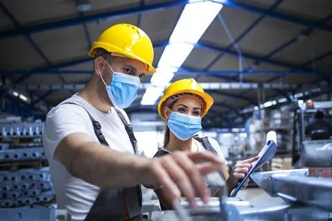 戴着防冠状病毒口罩的工业工人讨论工厂金属零件 戴着防冠状病毒口罩的工业工人讨论工厂金属零件